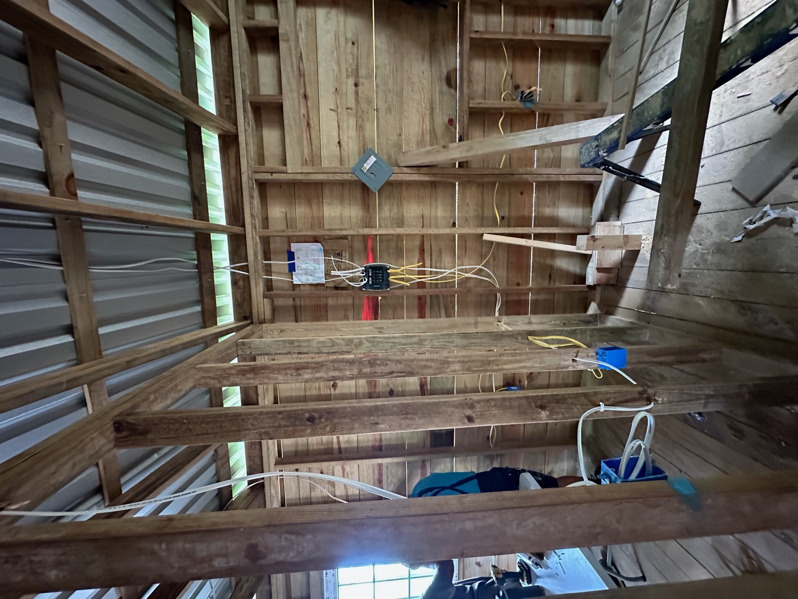 Wire runs and the electrical panel box mounted on the framed wall, with the wiring plan taped above it