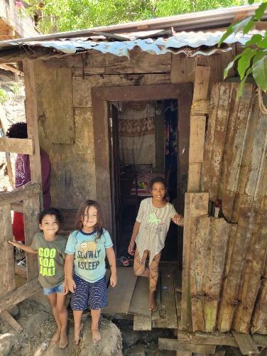 Children standing in the doorway of Candida's scrap-wood home in Roatán — the family RVT students will build a new home for this September